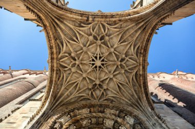 Closeup view of a medieval cathedral's entrance from ground up under blue skies with fluffy white clouds clipart