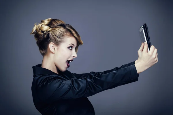 Portrait of a young woman, profile, taking a picture with her touch pad