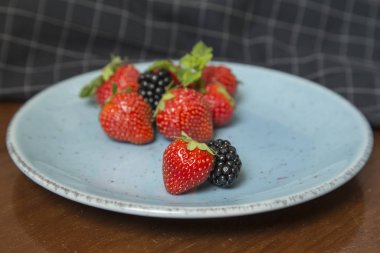 Mavi bir tabakta çilek ve böğürtlen.