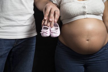Baba ve hamile anne el ele tutuşuyorlar ve gelecekteki bebeğin pembe ayakkabılarını tutuyorlar. Renkli fotoğraf.