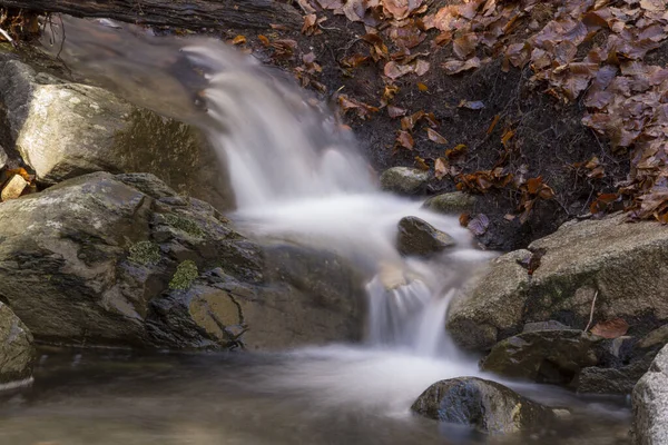 Detail of a waterfall between rocks of a mountain river with dry leaves on the river bank.