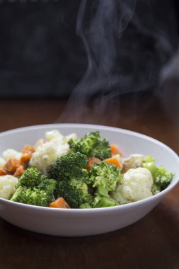 Kaynamış sebzeli buhar tabağı (havuç, brokoli ve karnabahar) siyah arka plan dikey bir resimde. Sağlıklı gıda konsepti.