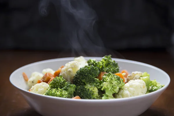 Steaming plate with boiled vegetables (carrots, broccoli and cauliflower) on a black background Gastro-photography concept.