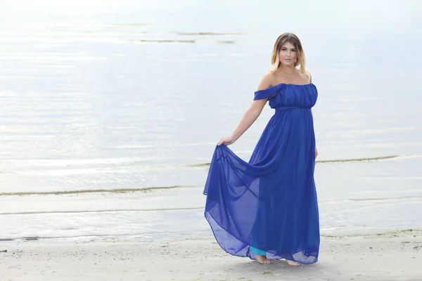 Woman in long dress sits on sand beach — Stock Photo, Image