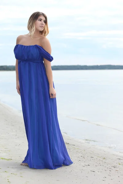 Жінка в довгій сукні сидить на піщаному пляжі — стокове фото
