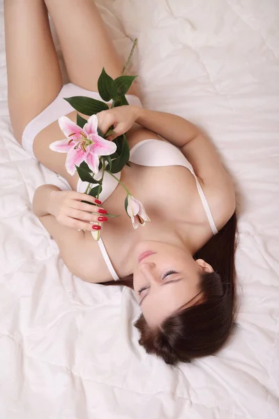 Mädchen in weißen Dessous und Lilie auf dem Bett — Stockfoto