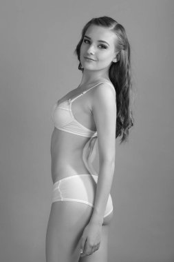 İnce vücutlu genç bir kadın iç çamaşırlarıyla poz veriyor.