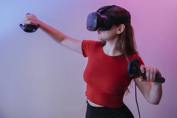 Kırmızı ceketli kahverengi saçlı bir kadın sanal gerçeklik oynar. Oda neon renklerle dolu.