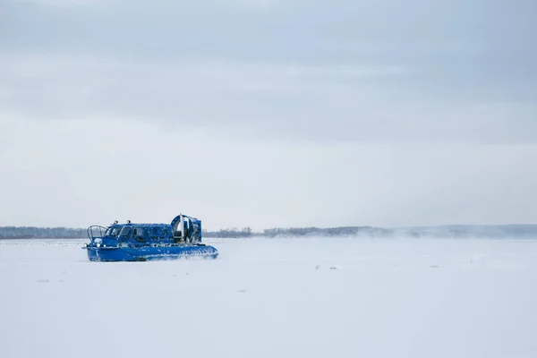 Po zamrzlém ledu řeky Volhy se řítí modré vznášedlo. Za ní se zvedá ze sněhu. — Stock fotografie
