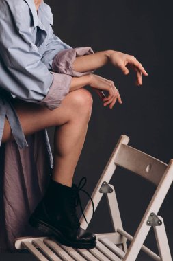 İki kol ve bir bacak. Elleri birbirine kenetlenmiş. Bacak, sandalyede ayakkabıyla duruyor. Sandalye beyaz. Bir adamın üzerinde mavi bir pelerin var..