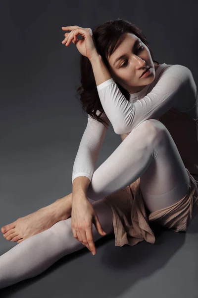 Kız LPG masajı için takım elbise giymiş ve elleri ve bacakları birbirine kenetlenmiş. Gri arkaplanda stüdyo çekimi