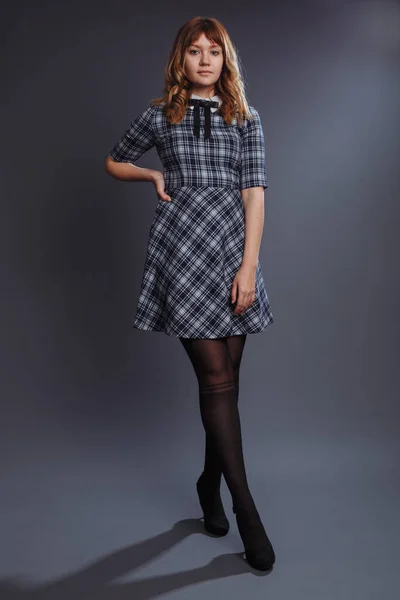 The girl is standing in a confident pose with her legs crossed. The girl in a blue dress in a large ruffle. Tights have a stocking pattern. Studio shot.