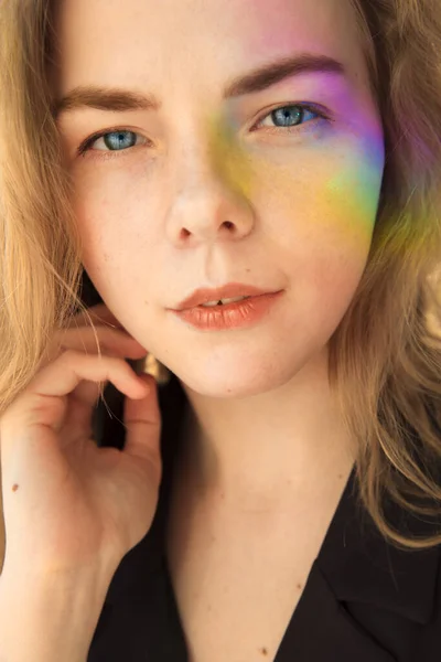 Portrait of a blue-eyed girl. She has a milky facial features. A rainbow of saturated colors falls on the face. — Stock fotografie