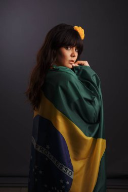 Esmer, çerçeveye arkadan bakıyor. Brezilya bayrağına sarılmış bir kız.