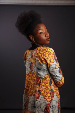 Ulusal bir kostümle göz kamaştırıcı saç stili olan güzel Afrikalı kız stüdyoda arkadan görünüyor.