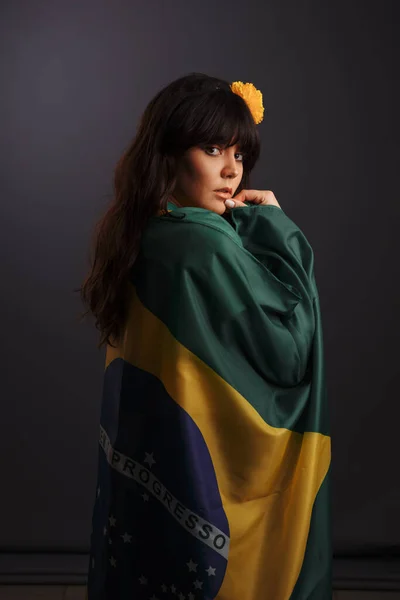 A morena olha para a moldura por trás. Uma menina embrulhada na bandeira do Brasil . — Fotografia de Stock