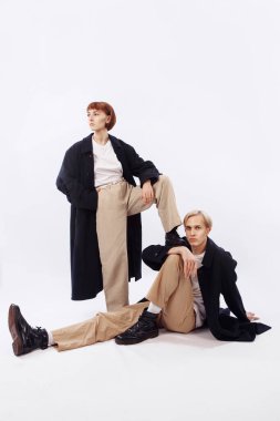 Kız ve erkek 90 'ların tarzında giyinmişler. Adam yerde oturuyor ve çerçeveye bakıyor. Bir kız bir erkeğin yanında duruyor. Kızların bacağı erkeklerin omuzunda..