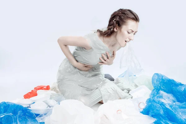 Мир задыхается от пластика. Девушка сидит на полу в пластиковом пакете. Мусор разбросан по девочке . — стоковое фото