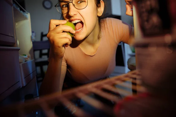 Gece atıştırması. Buzdolabındaki kıza bak. Kız buzdolabına uzandı ve yeşil bir elma yedi..