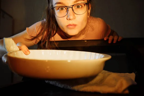 Вид из духовки. Девушка достает стеклянную сковороду из духовки. Человек освещается светом от духовки лампы . — стоковое фото