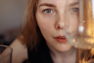 Açık renk saçlı ve sarı gözlü bir kız seyirciye şaşkınlıkla bakar. Bir cam kap kızın gözlerini kapatır.. 