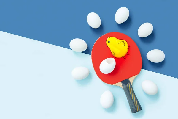 Bir tavuk da olabilirdi. Kırmızı masa tenisi raketi mavi masada yatıyor. Raketin etrafında aynı yumurtalar var.. — Stok fotoğraf