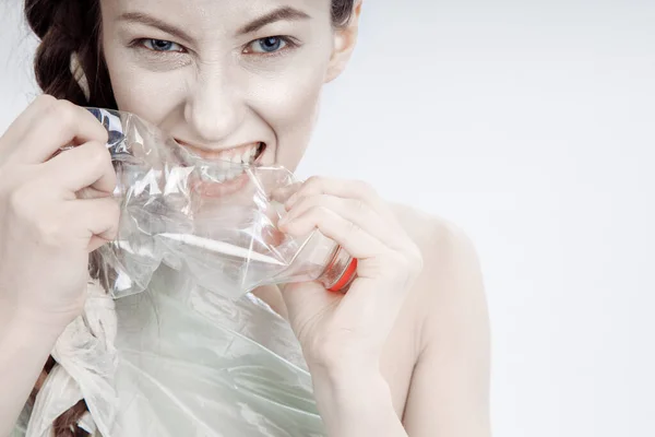 Девушка пытается разбить пластиковую бутылку зубами и руками. Женский пол агрессивно обнажает зубы . — стоковое фото