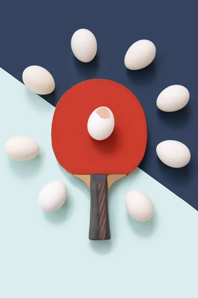 Kırmızı masa tenisi raketi ortada. Raketin üzerinde kırık bir yumurta var. Etrafta bir sürü yumurta var.. — Stok fotoğraf