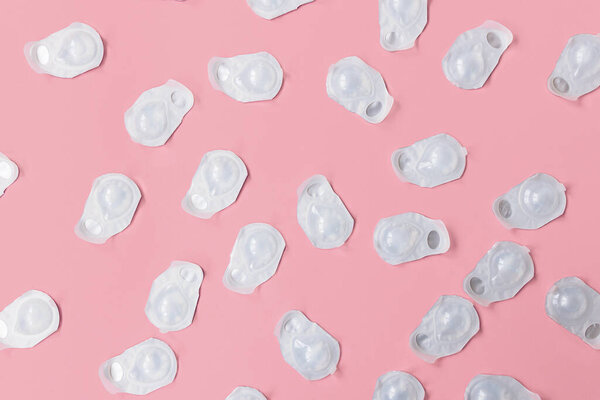 A lot of blisters with contact lenses interspersed on a pink background. Blisters are new and not open. 