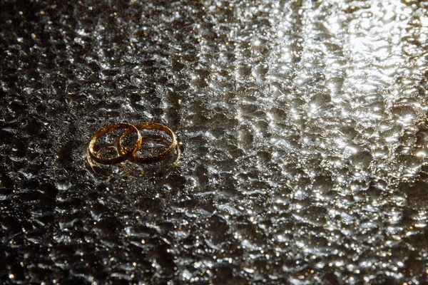 İki alyans büyük yağmur damlalarında yatar. Gece ışığında parlayan yağmur damlaları. 