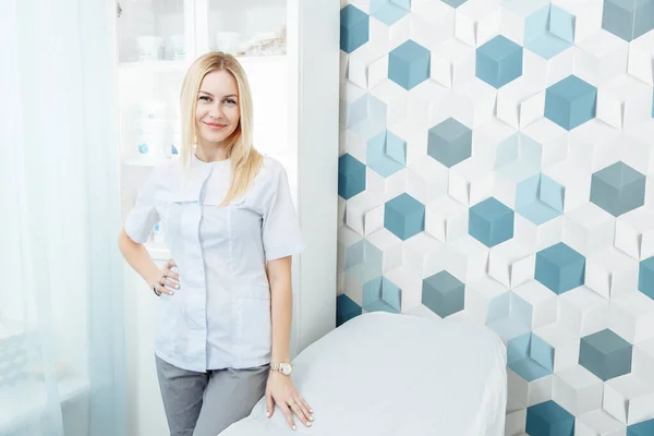 Güzel sarışın bir kız masaj masasının yanında duruyor..