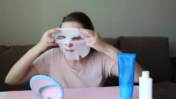 家の服を着たブルネットの女の子はファブリックフェイスマスクをつけます. — ストック動画