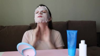 Esmer bir kadın kendine boyun masajı yapıyor. Kız kumaştan bir maske takıyor.