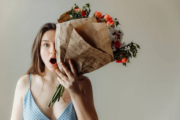 Удивлённая девушка закрывает часть лица букетом цветов. . — стоковое фото