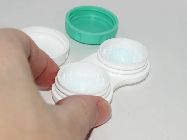 Gri bir arkaplan üzerinde yakın çekim çerçevesi içinde bir el ile görme düzeltmesi için kontak lensleri olan bir konteyner.