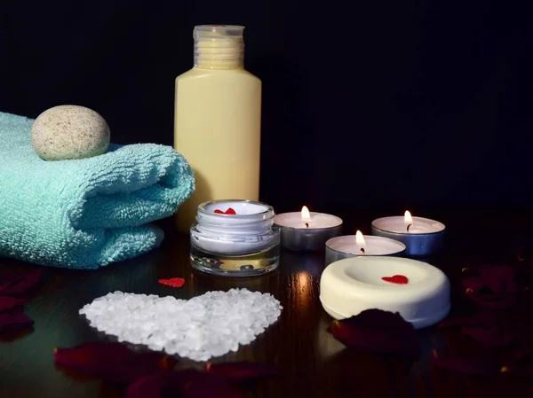 Valentine\'s day Spa style. a dark table on which one heart of bath salt is removed at 45 degrees with rose petals, a towel and cream. selective focus