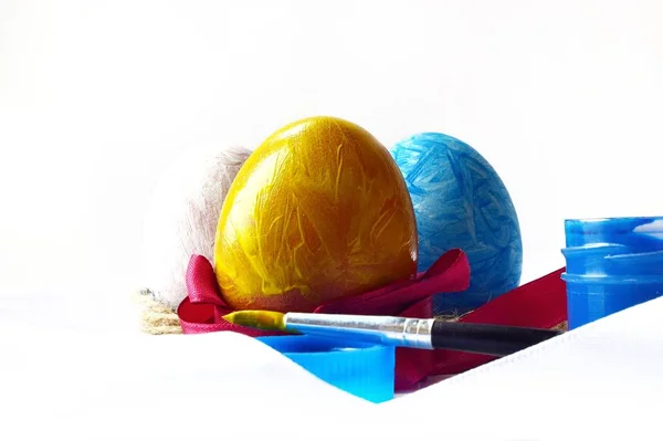 Açık arkaplanda saten kırmızı kurdele, fırça ve boya ile renklendirilmiş üç yumurta. Kapat. yumuşak odak