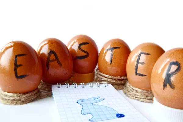 Paskalya yumurtalarının beyaz arka planda yazıldığı paskalya yumurtaları, üzerinde tavşan resmi olan bir Not Defteri sayfası. Kapat. yumuşak odak.