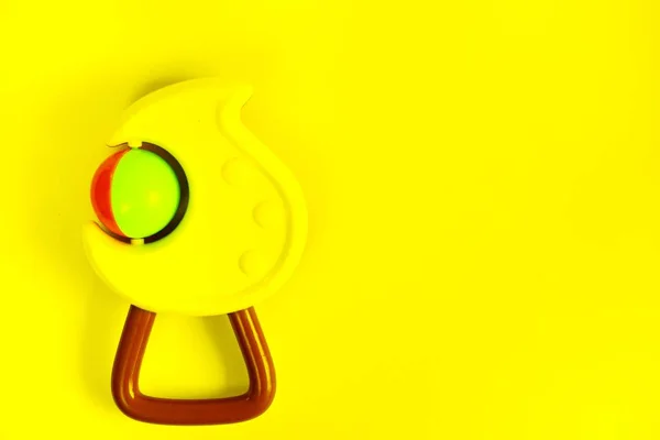 Sarı arka planda yeni doğanlar için bir çocuk çıngırak oyuncağı. Büyük planı izole et..