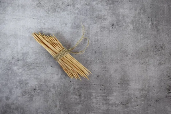 wooden toothpicks tied with a rope under the light of a tree on a concrete gray background . close up.