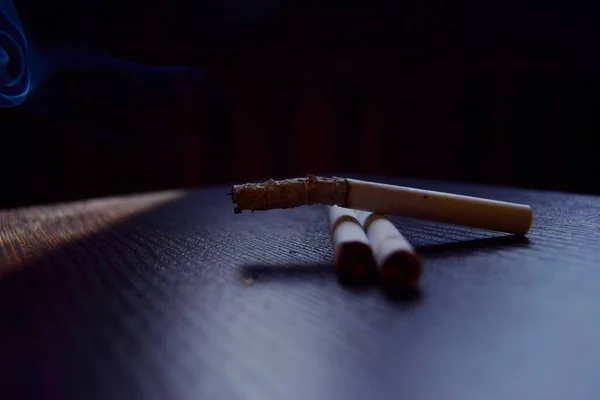 Karanlık masada üç dumanlı sigara var. Nikotinin sağlığa zararları. Kapat.