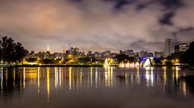 Brezilya, Sao Paulo 'da Akşam Işıkları. Gece Ibirapuera Parkı 'nı aydınlattı. Modern Gökdelenler, Gölün Yansıması ve Su Çeşmesi.