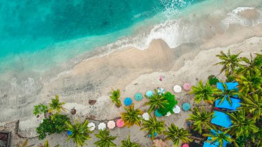 Palmiyeler, güneş şemsiyeleri, Bali ve Endonezya ile deniz ve kumlu sahilin inanılmaz manzarası.