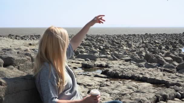 一个女人坐在海滩上 凝视着远方的大海 凝视着鸟儿 一个女人坐在海滩上 端着一杯咖啡 用一只手捧着鸟儿 — 图库视频影像