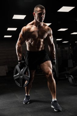 Yakışıklı ve kaslı bir adam, spor salonunda kameraya poz veriyor.