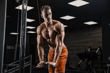 Yakışıklı ve kaslı bir adam, spor salonunda kameraya poz veriyor.