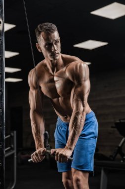 Yakışıklı ve kaslı bir adam, spor salonunda kameraya poz veriyor.