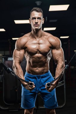 Yakışıklı ve kaslı bir adam, spor salonunda kameraya poz veriyor.