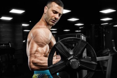 Yakışıklı ve kaslı bir adam, spor salonunda kameraya poz veriyor.