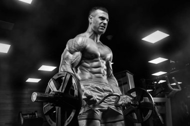 Yakışıklı ve kaslı bir adam, spor salonunda kameraya poz veriyor.